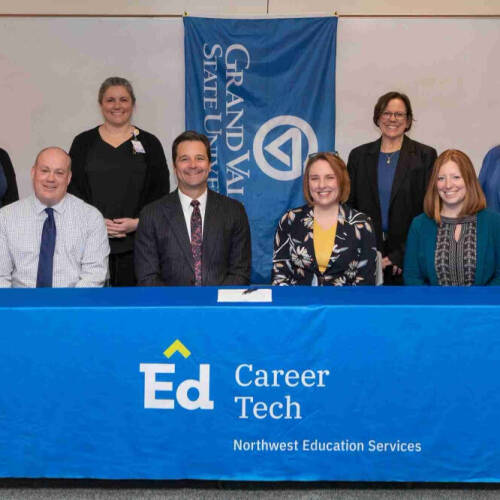 A group of eight people pose in front of a blue banner and tablecloth with university and career tech branding.